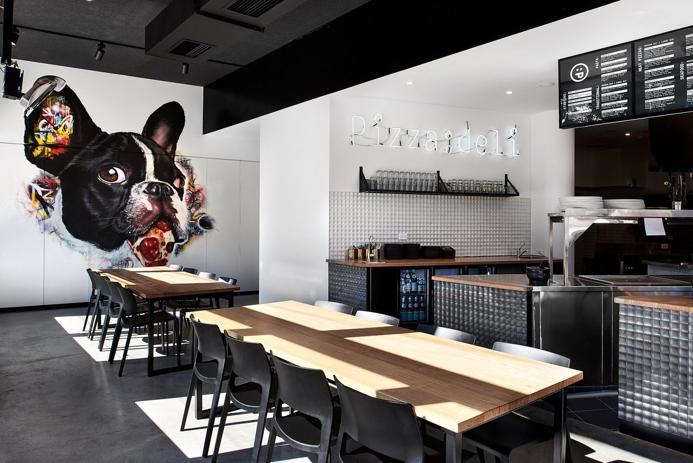 Full dining room with neon sign and dog mural at Pizza:deli